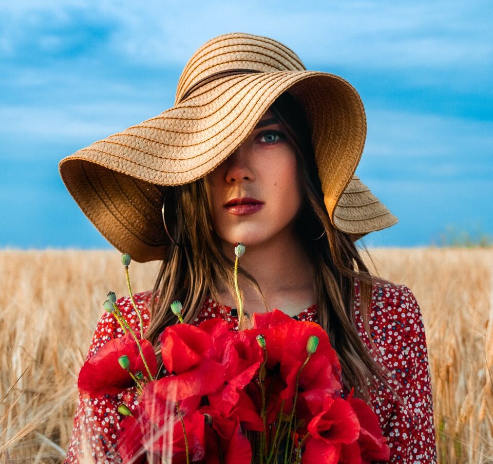 woman in brown straw hat holding red flowers